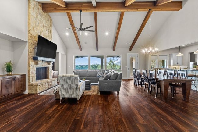 Living area with ceiling fan with notable chandelier, dark wood-style floors, a fireplace, and high vaulted ceiling | Image 5