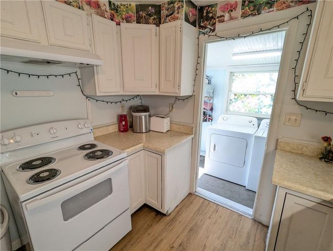 Kitchen featuring white electric range, light countertops, washer and dryer, light wood-style flooring, and white cabinetry | Image 17