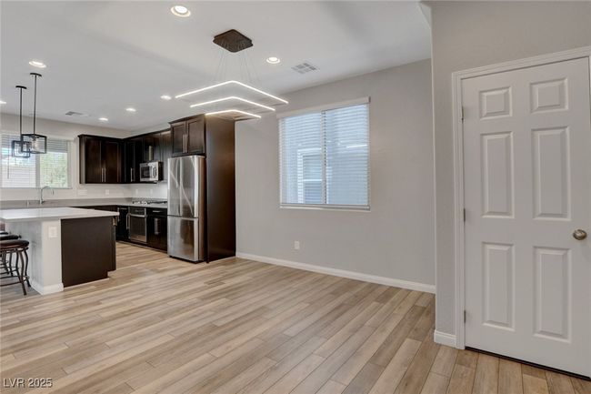Kitchen with appliances with stainless steel finishes, light countertops, light wood-type flooring, a breakfast bar, and dark brown cabinets | Image 6