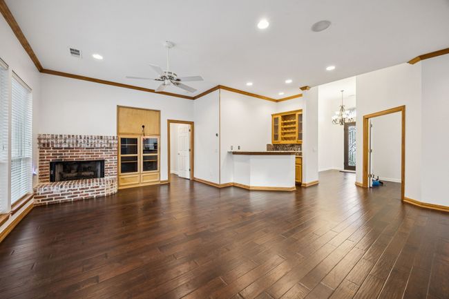 Living room with a brick fireplace, plenty of natural light, dark wood finished floors, baseboards, recessed lighting and wet bar | Image 7