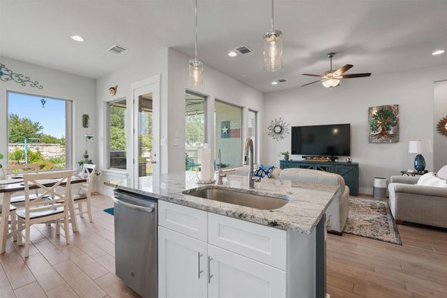 Kitchen featuring stainless steel dishwasher, a sink, open floor plan, light wood-style floors, and light stone counters | Image 7