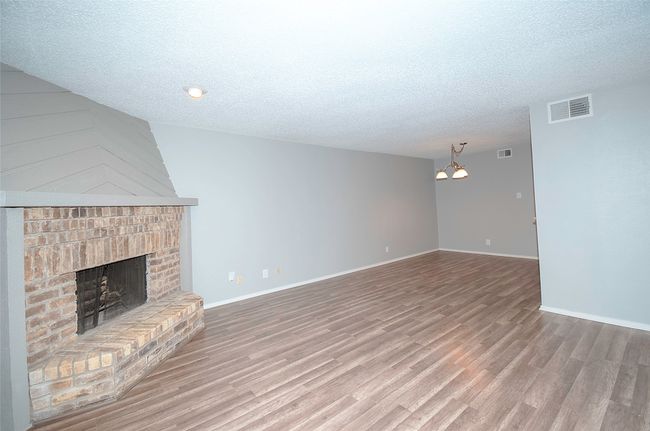 Unfurnished living room with a textured ceiling, an inviting chandelier, hardwood / wood-style floors, and a brick fireplace | Image 13