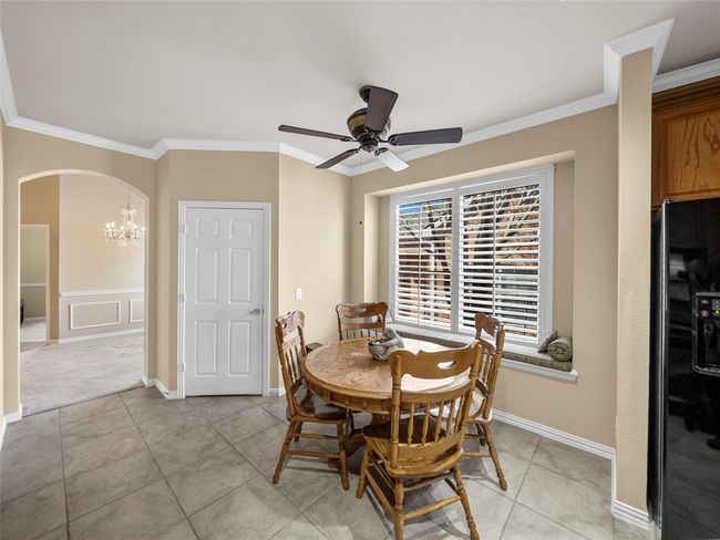 Dining area featuring ceiling fan with notable chandelier, arched walkways, crown molding, and light tile patterned floors | Image 7
