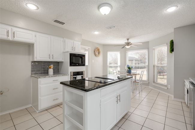 Kitchen with light tile patterned floors, visible vents, a kitchen island, black appliances, and backsplash | Image 14