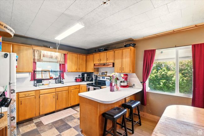 Kitchen featuring stainless steel range with electric cooktop, a sink, under cabinet range hood, light countertops, and a peninsula | Image 6