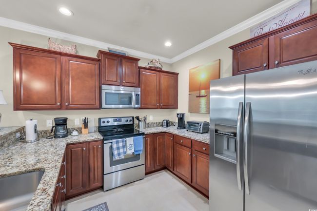 Kitchen with appliances with stainless steel finishes, crown molding, light stone countertops, recessed lighting, and reddish brown cabinets | Image 8