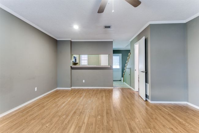 Empty room with light wood-style floors, ceiling fan, ornamental molding, and a textured ceiling | Image 7