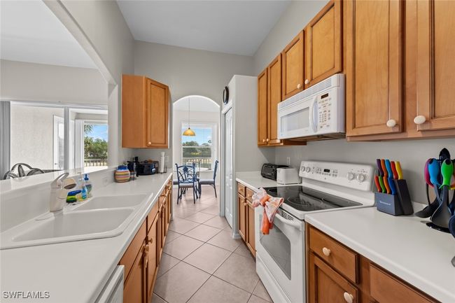 Kitchen with a sink, brown cabinets, white appliances, light tile patterned floors, and light countertops | Image 10
