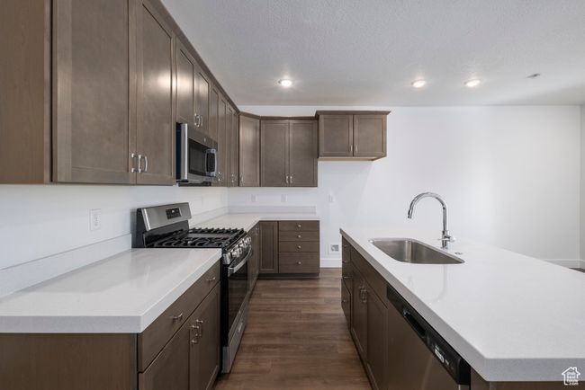 Kitchen with an island with sink, light countertops, dark wood-style floors, stainless steel appliances, and a sink | Image 6