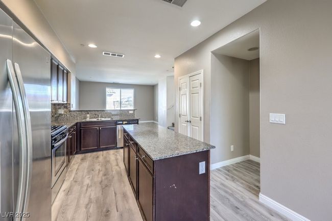 Kitchen featuring light wood-type flooring, stainless steel appliances, baseboards, visible vents, and dark brown cabinets | Image 12