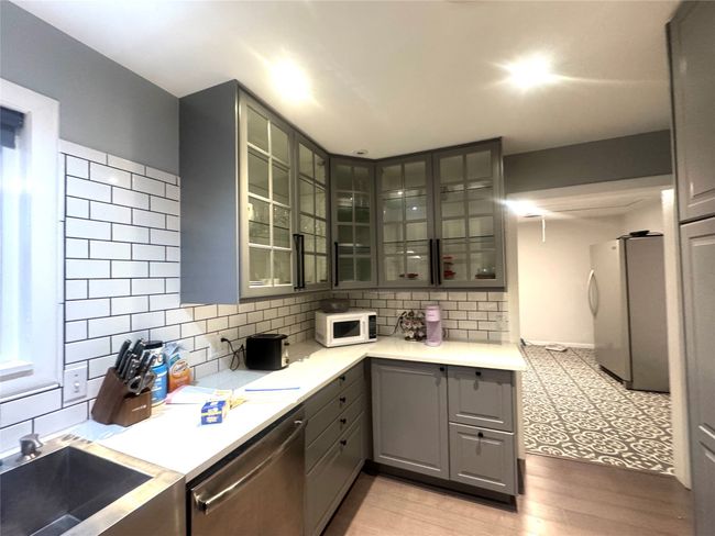 Kitchen with gray cabinets, dishwasher, white microwave, freestanding refrigerator, and glass insert cabinets | Image 8
