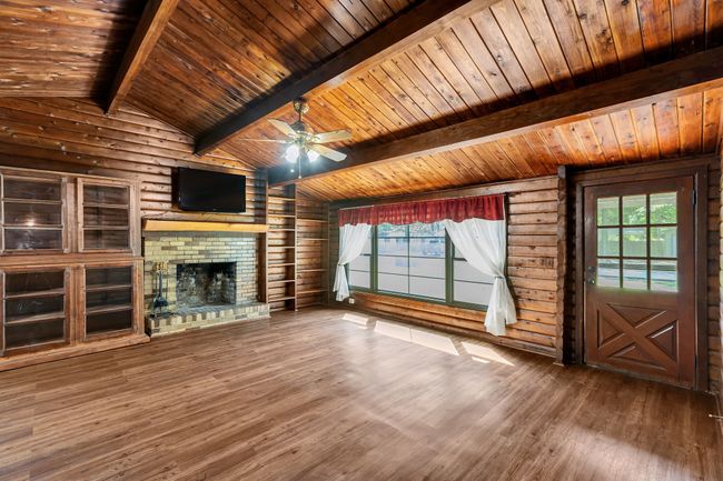 iving room with a brick fireplace, wood finished floors, a ceiling fan, rustic walls, and wood ceiling | Image 6