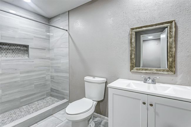 The modern bathroom features a beautifully tiled shower with hexagon tile accents for a luxurious touch. A sleek vanity with a framed mirror adds rustic charm to the contemporary design, making this space both functional and elegant. | Image 13