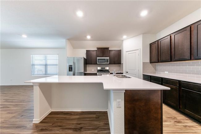 Kitchen with appliances with stainless steel finishes, dark brown cabinets, an island with sink, light wood-type flooring, and recessed lighting | Image 4