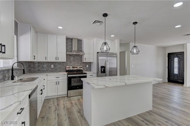 Kitchen featuring stainless steel appliances, wall chimney exhaust hood, a sink, a kitchen island, and light wood-type flooring | Image 12