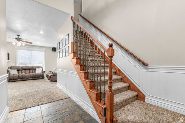 Stairs featuring a decorative wall, wainscoting, stone tile flooring, a ceiling fan, and a textured ceiling | Image 15