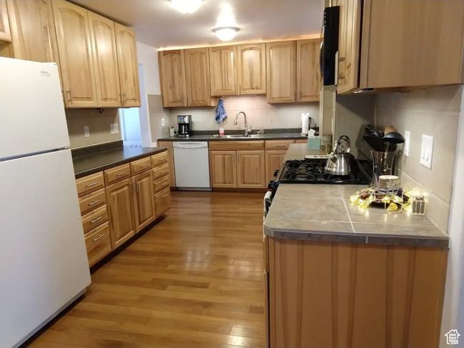 Kitchen featuring tasteful backsplash, white appliances, a sink, light wood-style floors, and light brown cabinets | Image 5
