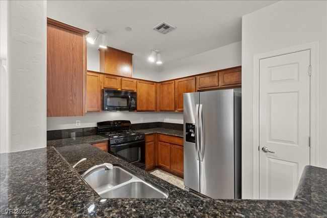 Kitchen with black appliances, brown cabinetry, and dark stone counters | Image 8