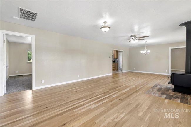 Unfurnished living room featuring a wood stove, light wood-type flooring, ceiling fan, and a chandelier | Image 13