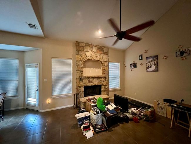 Tiled living room featuring ceiling fan, plenty of natural light, vaulted ceiling, and a stone fireplace | Image 8