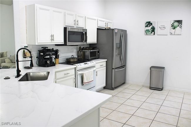 Kitchen featuring light tile patterned floors, white cabinets, light stone countertops, stainless steel appliances, and a sink | Image 5
