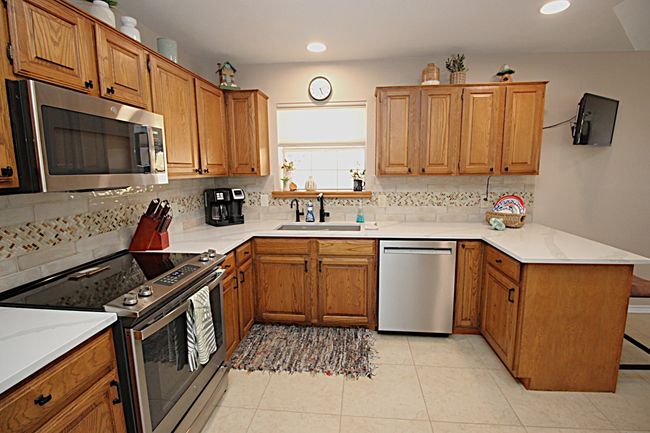 Kitchen with brown cabinets, a sink, stainless steel appliances, a peninsula, and decorative backsplash | Image 20