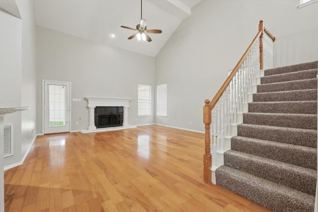 Unfurnished living room featuring high vaulted ceiling, a tiled fireplace, stairs, ceiling fan, and light wood-type flooring | Image 5