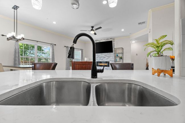 Kitchen view of crown molding, a fireplace, ceiling fan, light stone counters, and pendant lighting | Image 13