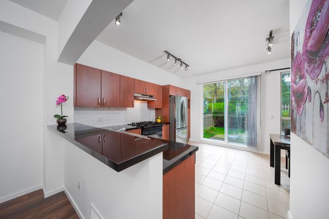 Kitchen featuring dark countertops, freestanding refrigerator, a peninsula, under cabinet range hood, and rail lighting | Image 11