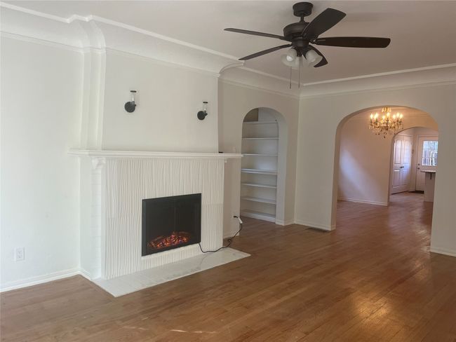 Unfurnished living room with arched walkways, built in features, wood finished floors, baseboards, and crown molding | Image 7