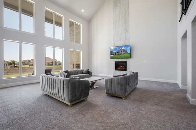 Carpeted living room featuring a towering ceiling, a tiled fireplace, plenty of natural light, baseboards, and recessed lighting | Image 12