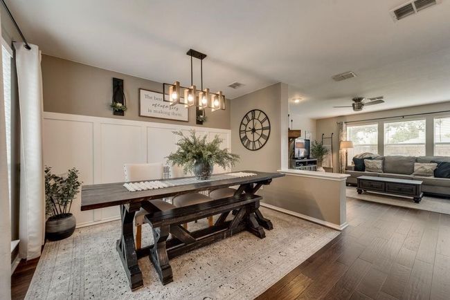 Dining area with dark wood-style floors, a decorative wall, a wainscoted wall, a ceiling fan, and a chandelier | Image 9