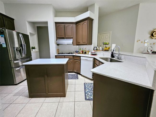 Kitchen featuring stainless steel fridge with ice dispenser, white dishwasher, range hood, a peninsula, and light tile patterned flooring | Image 10