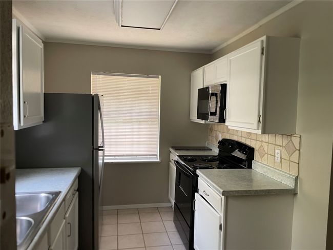 Kitchen featuring black appliances, tasteful backsplash, white cabinets, light tile patterned floors, and crown molding | Image 4