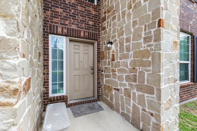 Charming entrance featuring a tan door surrounded by a mix of brick and stonework, with a small window and outdoor light fixture. | Image 4
