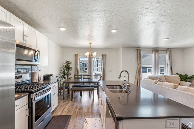 Kitchen featuring appliances with stainless steel finishes, dark countertops, a sink, a kitchen island with sink, and plenty of natural light | Image 12