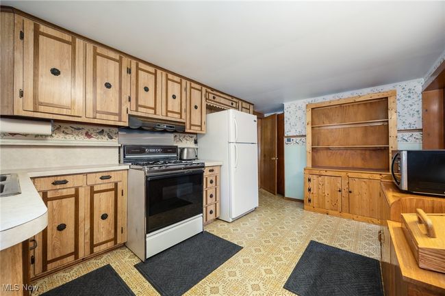 Kitchen with stainless steel microwave, under cabinet range hood, light countertops, wallpapered walls, and gas range | Image 8