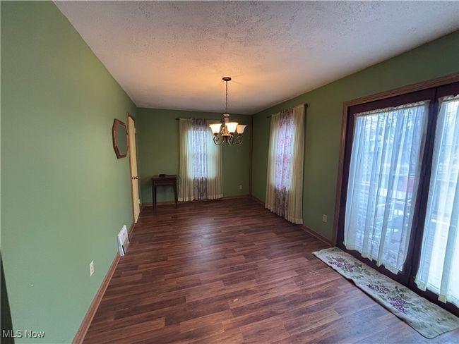 Unfurnished dining area featuring baseboards, visible vents, wood finished floors, a textured ceiling, and a notable chandelier | Image 5