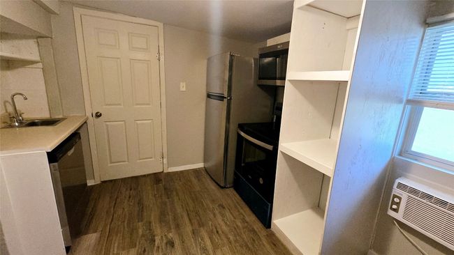 Kitchen with dark wood-style flooring, a sink, light countertops, an AC wall unit, and stainless steel appliances | Image 31
