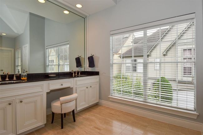 Primary bathroom featuring a large vanity with dual sinks, granite counters, ample cabinetry, and a built-in dressing table. There's a large window with blinds offering natural light | Image 19