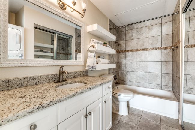 Full bathroom with stacked washer and clothes dryer, vanity, toilet, tile patterned floors, and shower / tub combination | Image 15