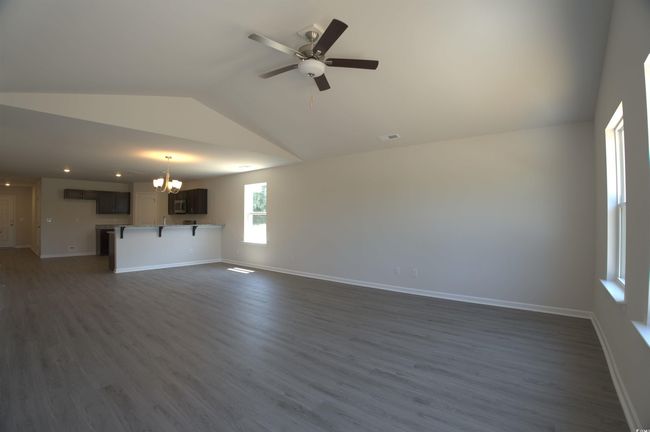 Unfurnished living room with vaulted ceiling, a chandelier, dark wood-style floors, and a ceiling fan | Image 4