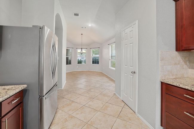 Kitchen featuring freestanding refrigerator, light tile patterned floors, vaulted ceiling, a chandelier, and light stone countertops | Image 14