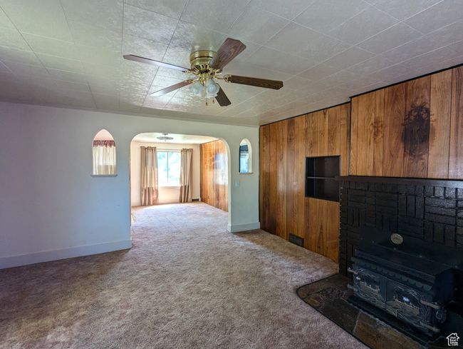 Unfurnished living room featuring wooden walls, ceiling fan, carpet flooring, a fireplace, and arched walkways | Image 4