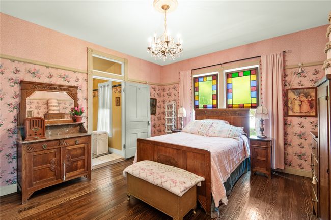 Bedroom featuring an inviting chandelier, wallpapered walls, and dark wood finished floors | Image 16