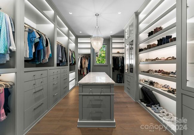 This primary walk-in closet features custom cabinetry and lit shelving. | Image 23