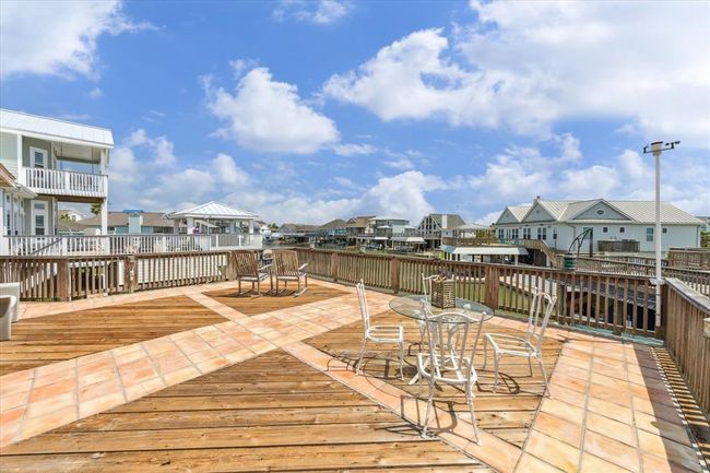 Spacious deck with a mix of wood and tile flooring. Surrounded by coastal-style homes under a bright blue sky, offering a relaxing outdoor space with scenic neighborhood views. | Image 8
