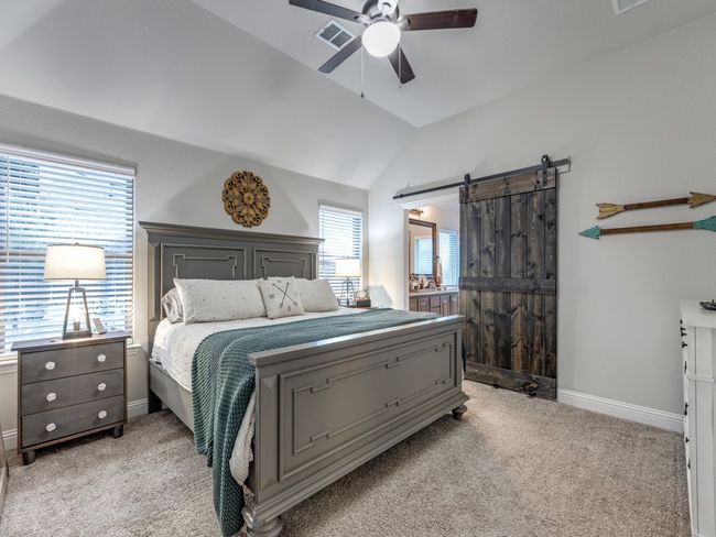 Carpeted bedroom featuring a barn door to the ensuite bathroom, lofted ceiling, and ceiling fan. | Image 9