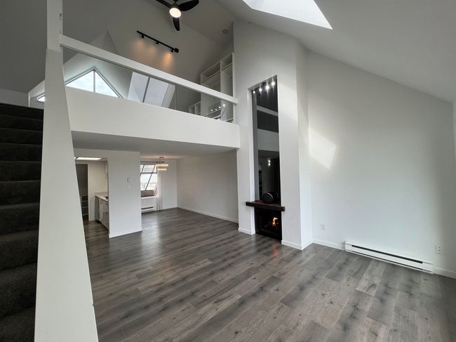 Unfurnished living room with baseboard heating, high vaulted ceiling, a skylight, stairs, and wood finished floors | Image 16
