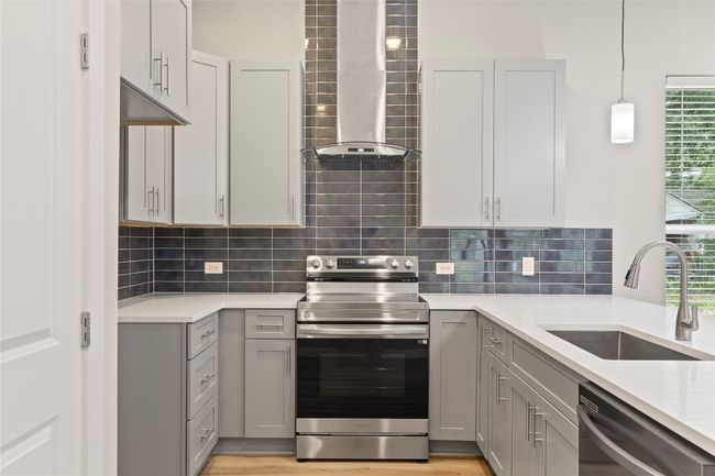 A stylish kitchen with stainless steel appliances, a sleek wall chimney range hood, elegant gray cabinetry, and plenty of natural light—perfect for culinary inspiration! | Image 9